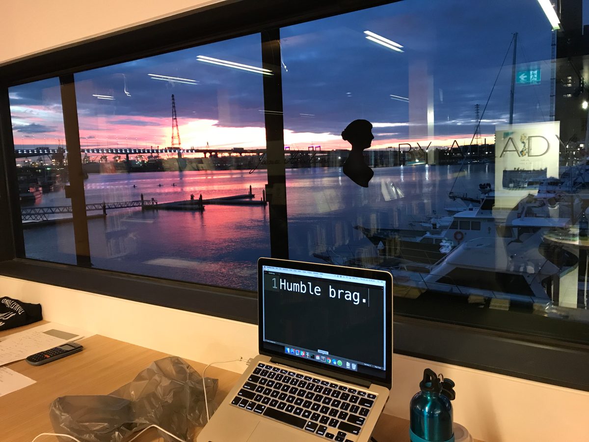 A view of a beautiful sunset over water through a window. A computer sits inside with "humble brag" showing on the screen.