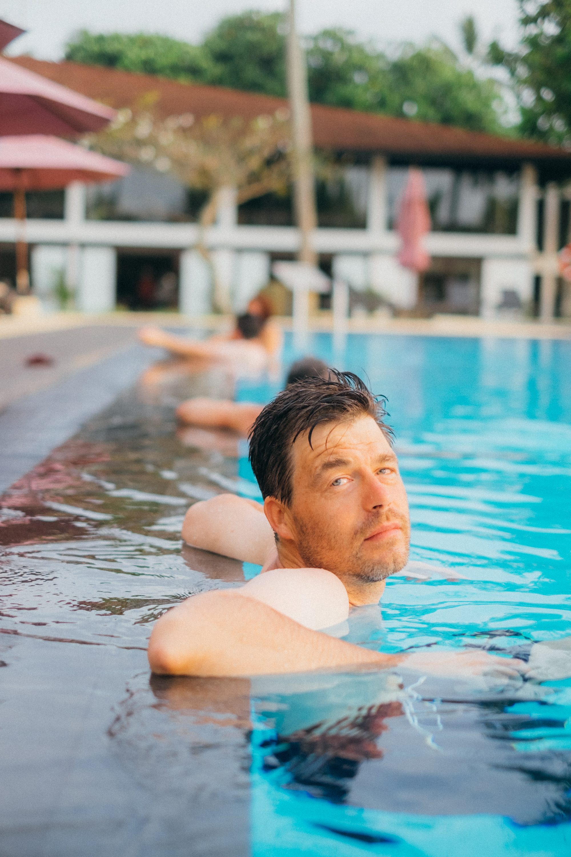 A thirst-trap photo of me in a pool relaxing against the pool-deck.