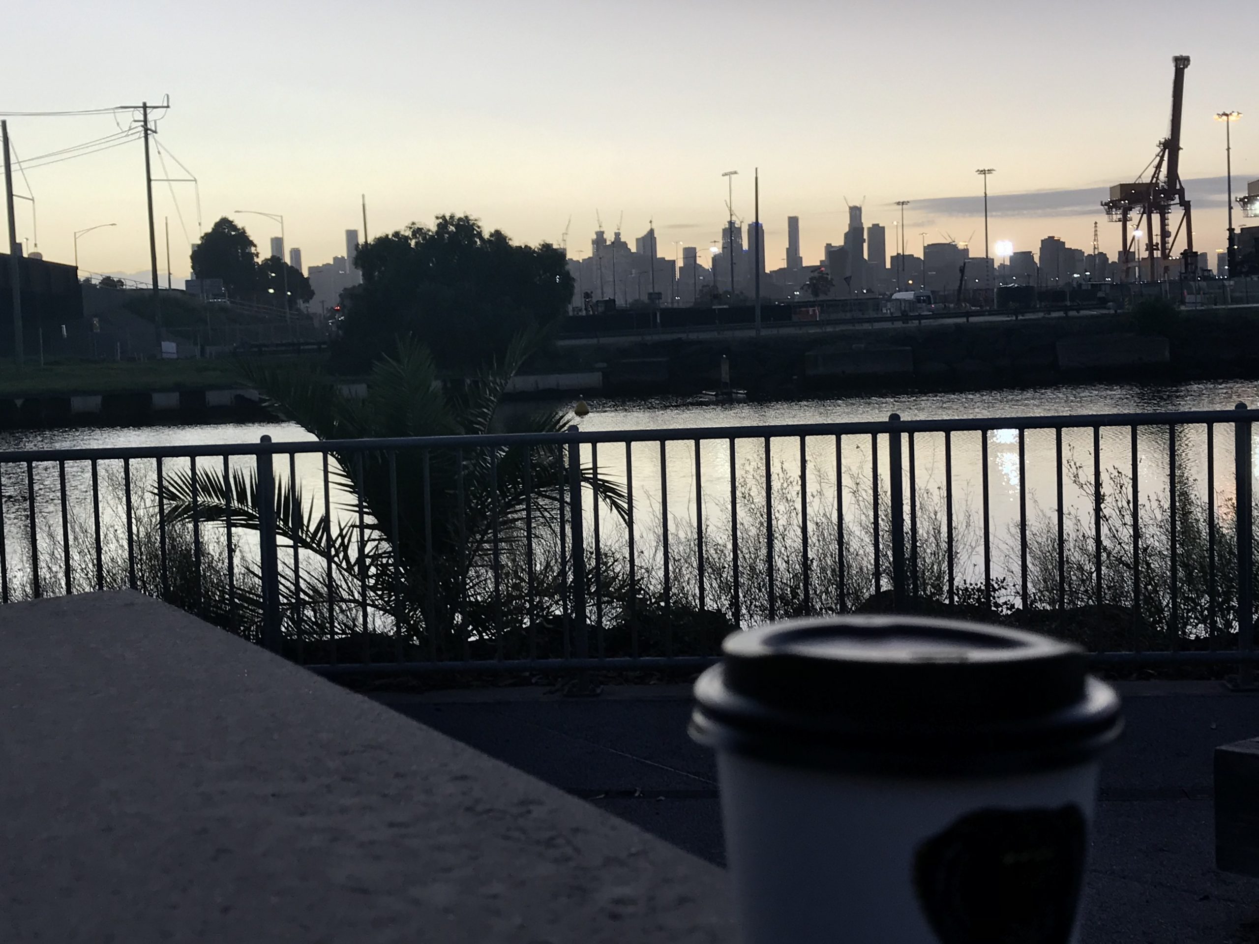 Photo of a river with a coffee cup in the foreground and the Melbourne city skyline in the background
