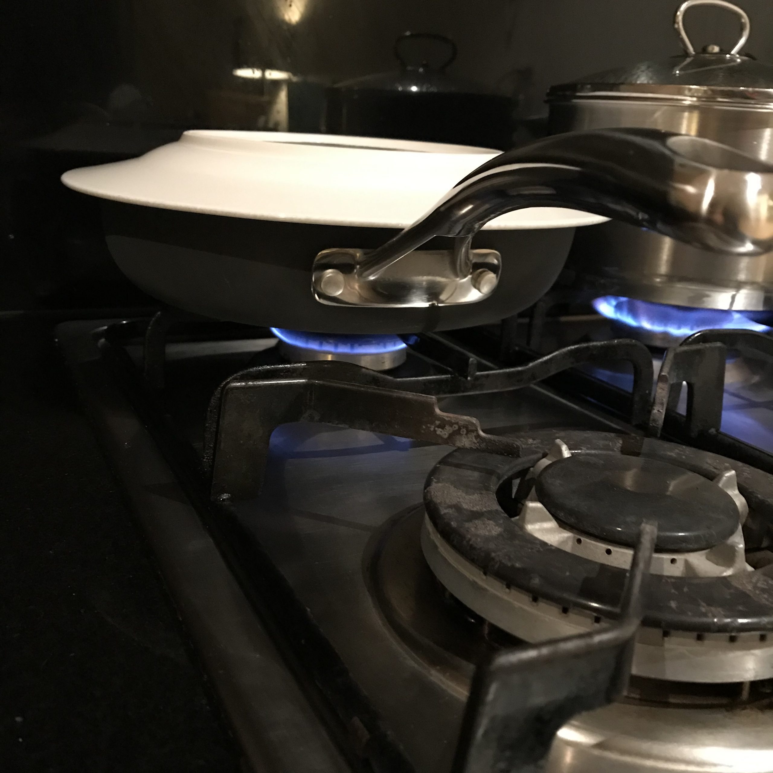 A fry pan on a stove top, the fry pan is covered with a ceramic plate