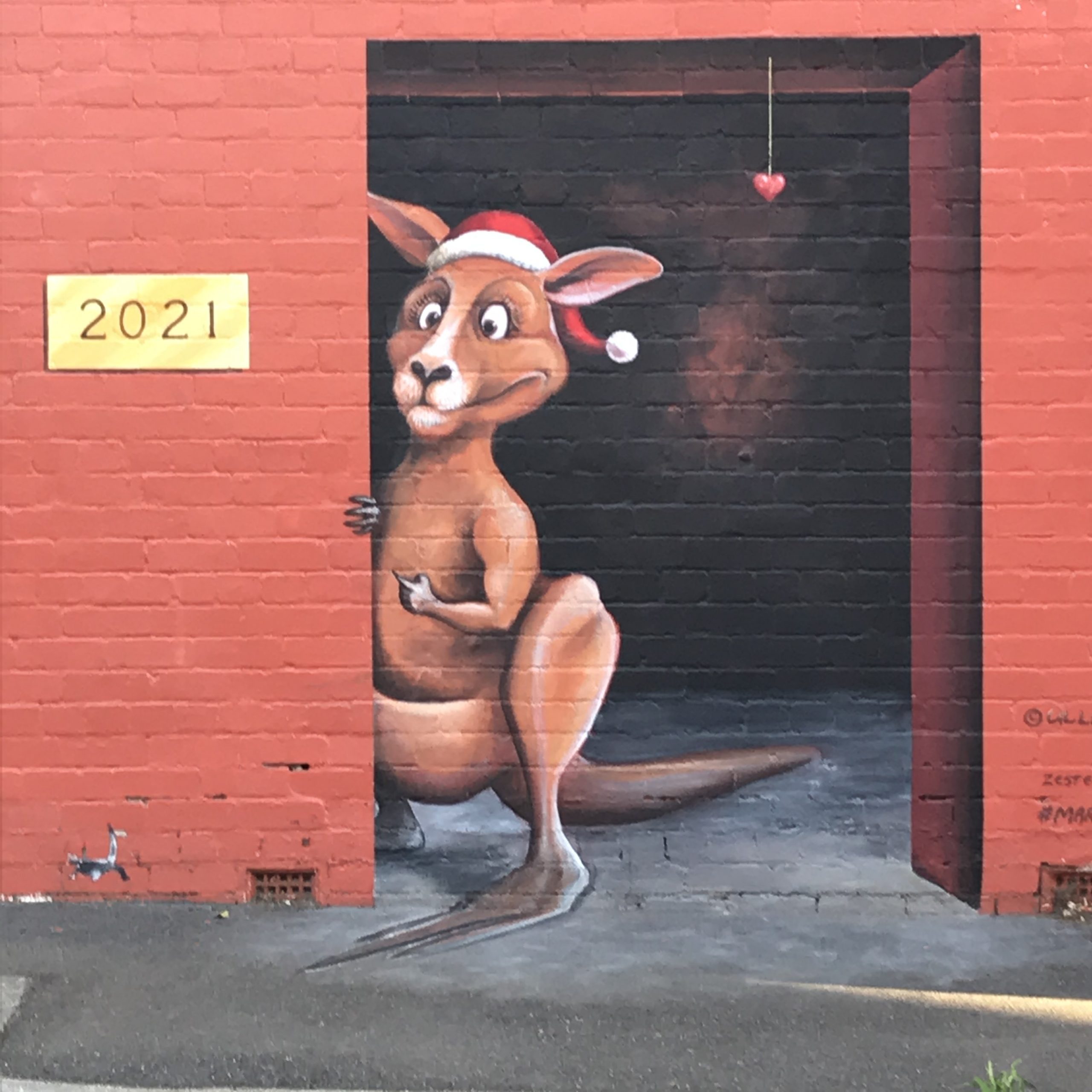 Street art of a kangaroo in a Santa hat looking out a door at a sign that says 2021
