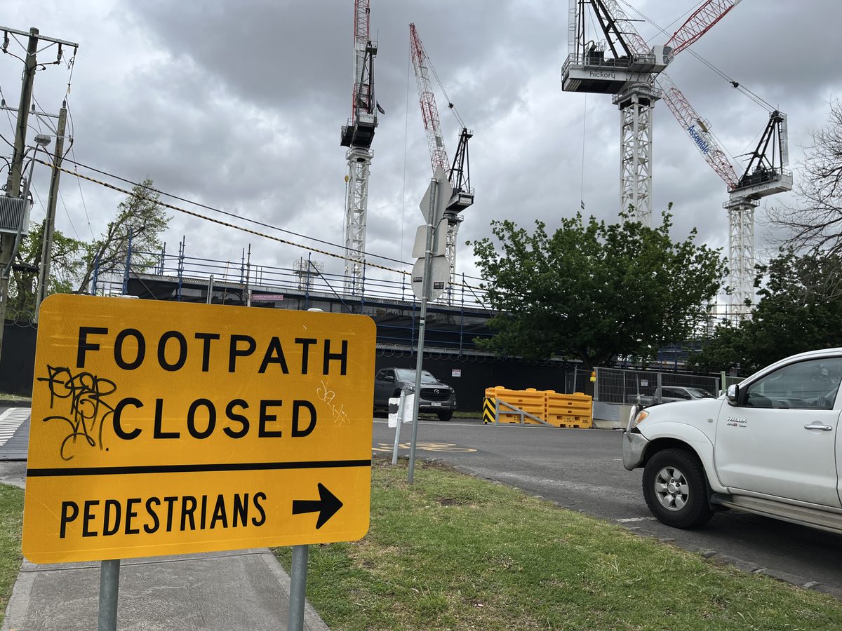 A permanent sign that says "footpath closed", directing pedestrians to the right. In the background is a large building site.