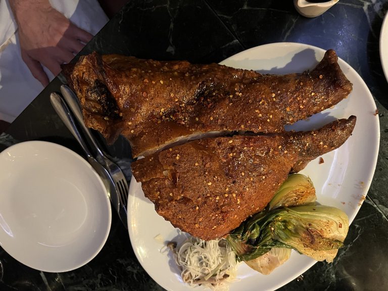 An entire cooked pig's head that has been deep fried with a herb rub resulting in a very crispy skin. There are some token greens, pak choy, on the plate but they are very small compared to the feature.